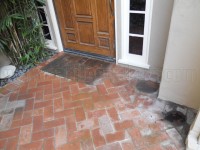 Exterior brick porch with ground in dirt and hard water deposits.
